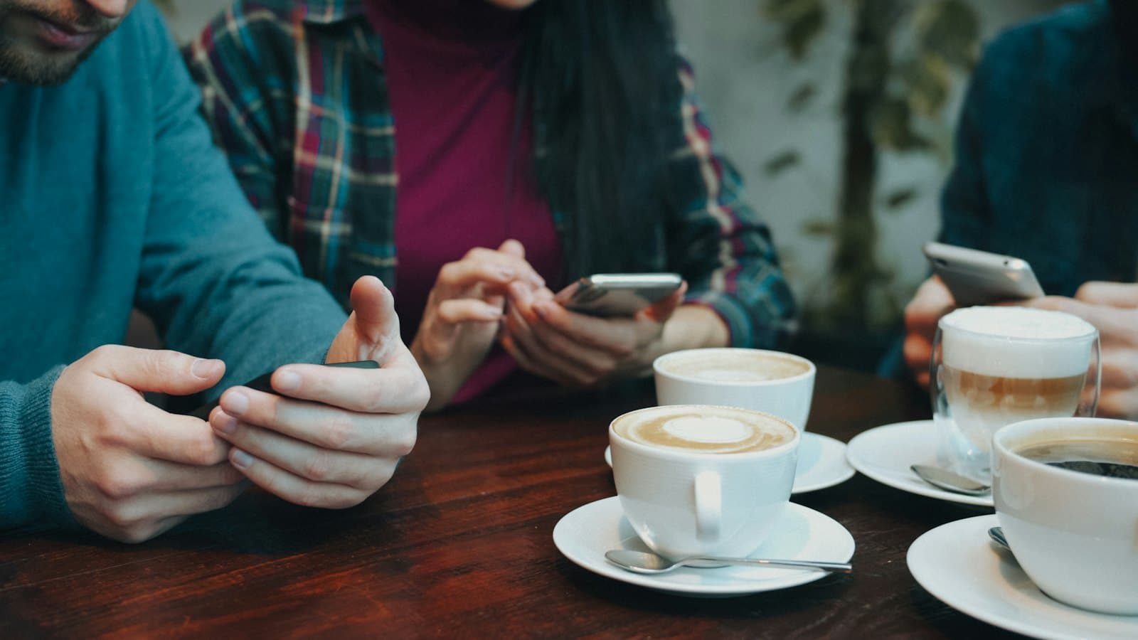 Venner ved et cafébord med kaffe og telefoner